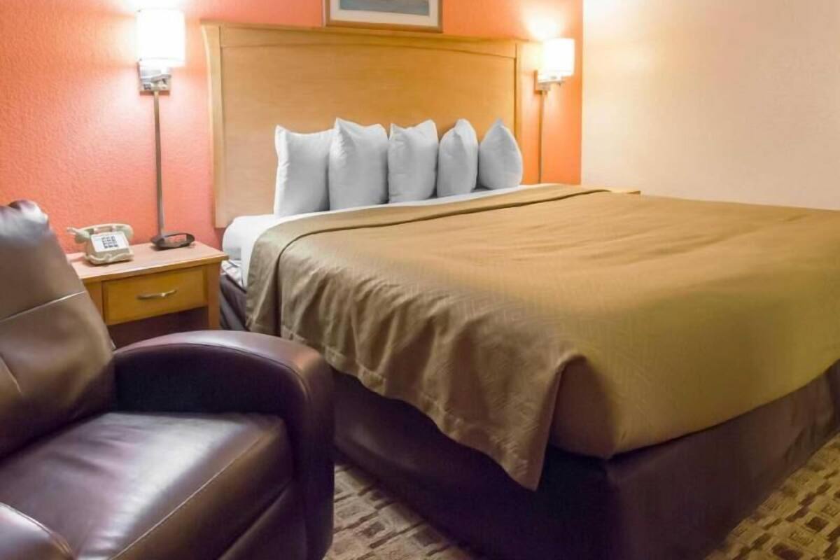 A hotel room with a bed, a nightstand with a telephone, a chair, and two wall-mounted lamps.