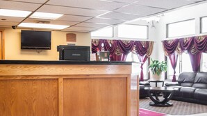 A reception area with a wooden counter, a flat-screen TV, and a Samsung printer. There is a leather sofa and a small table with a potted plant.