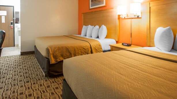 A hotel room with two beds, a headboard with a clock, a framed picture on the wall, and a carpeted floor.