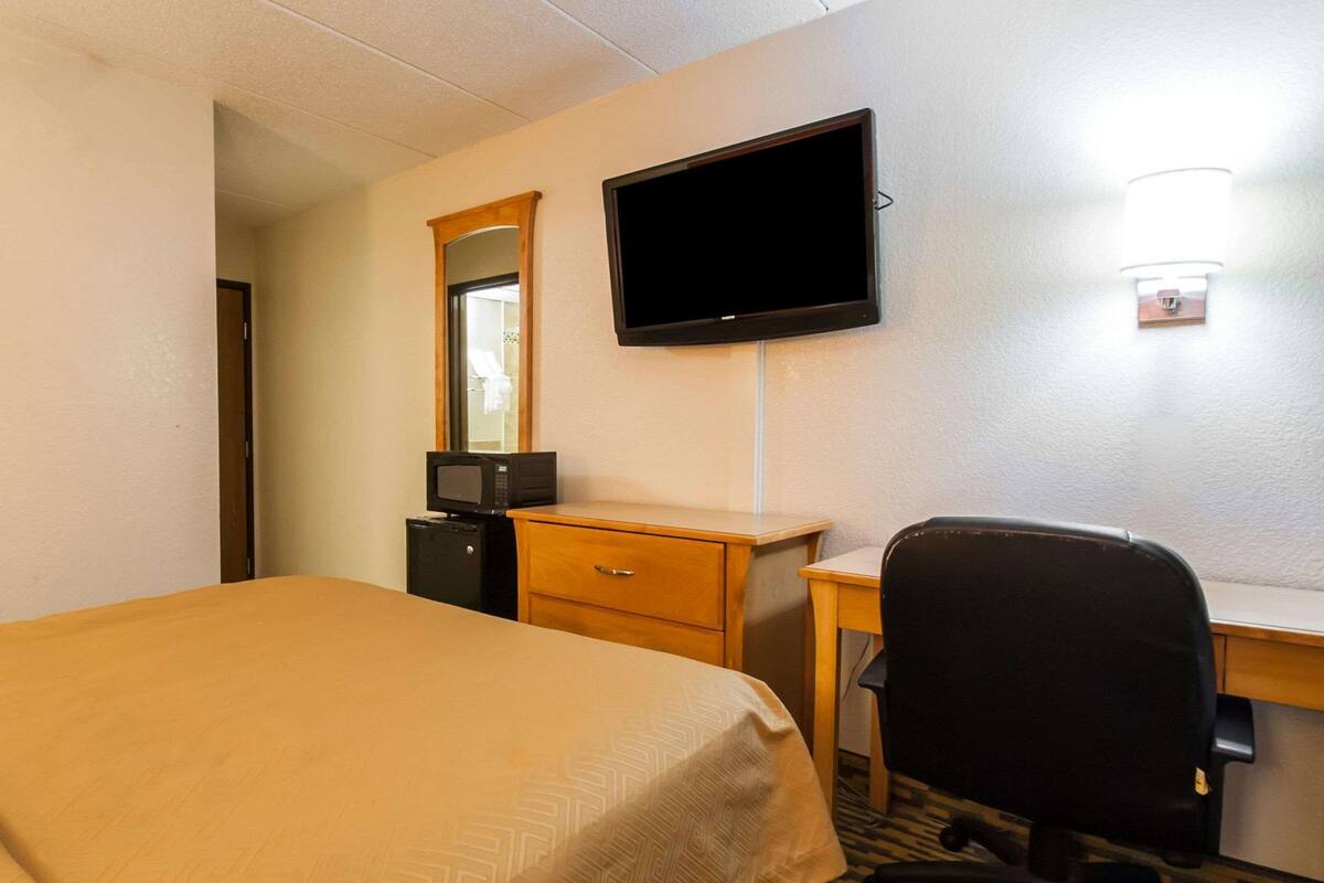 A hotel room with a bed, a desk, a chair, a television, and a mirror.