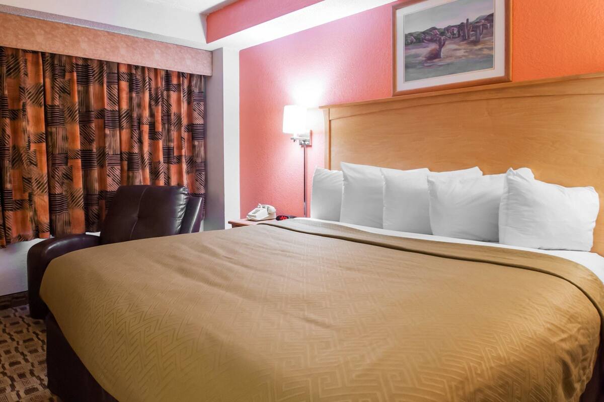 A hotel room with a large bed, a desk with a telephone, a chair, and a painting on the wall.