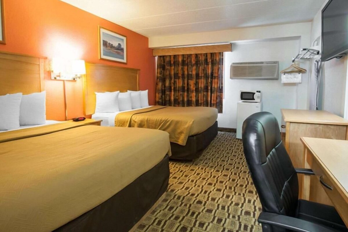 A hotel room with two beds, a desk, a chair, an air conditioning unit, and a television.