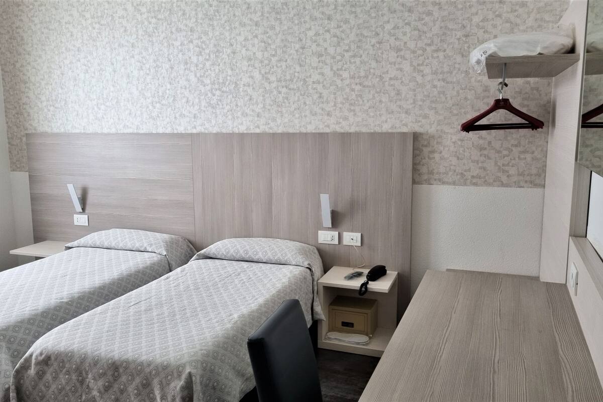 A twin room with two beds, a bedside table with a phone, a small cabinet, and a hanging clothes rack.