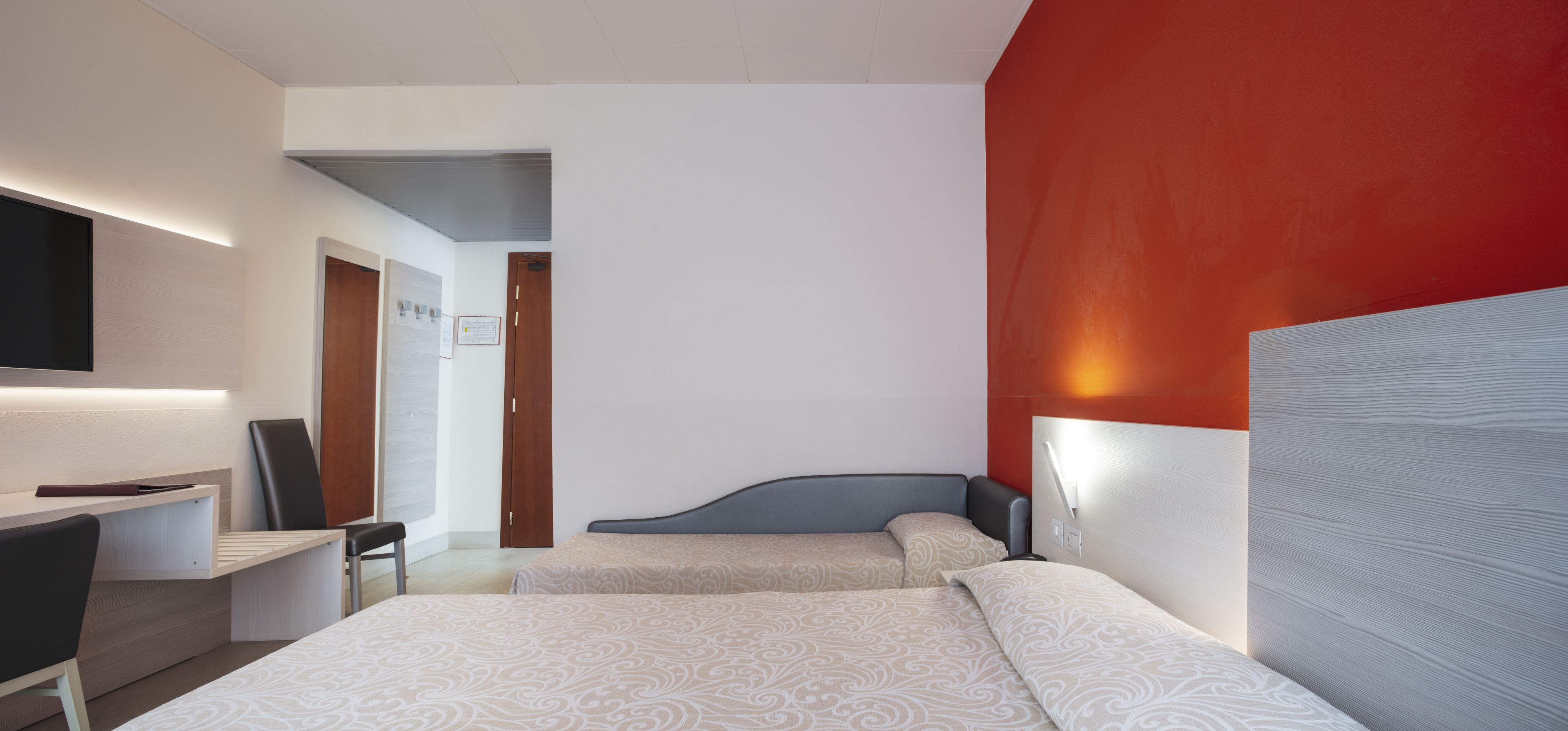 A modern hotel room with two beds, a desk, and a TV.