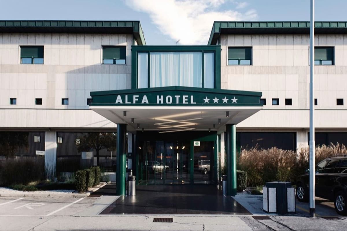 The exterior of the ALFA HOTEL with a covered entrance, parking area, and a clear sky.