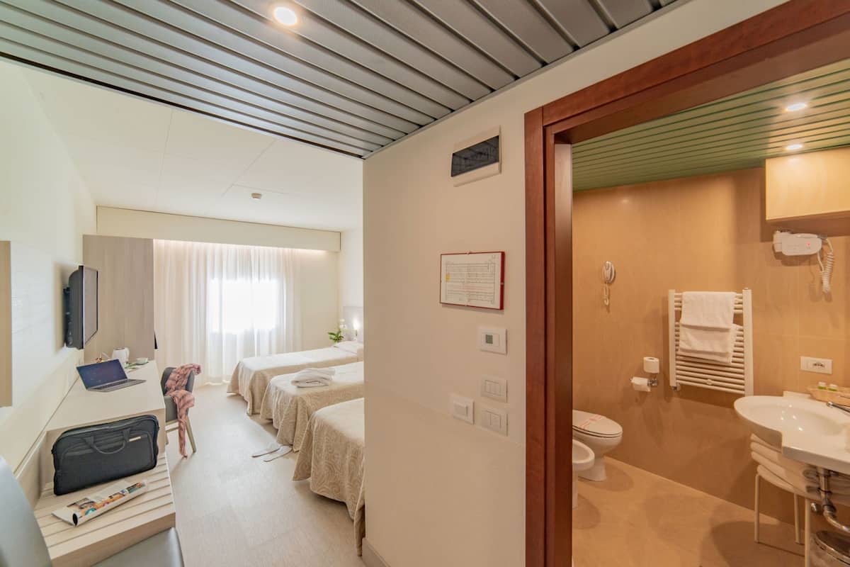 A hotel room with a desk, two beds, a shower, and a bathroom.