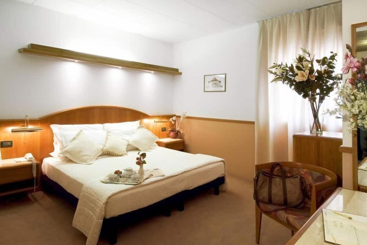 A hotel room with a bed, bedside table, lamp, chair, and a desk with a mirror.