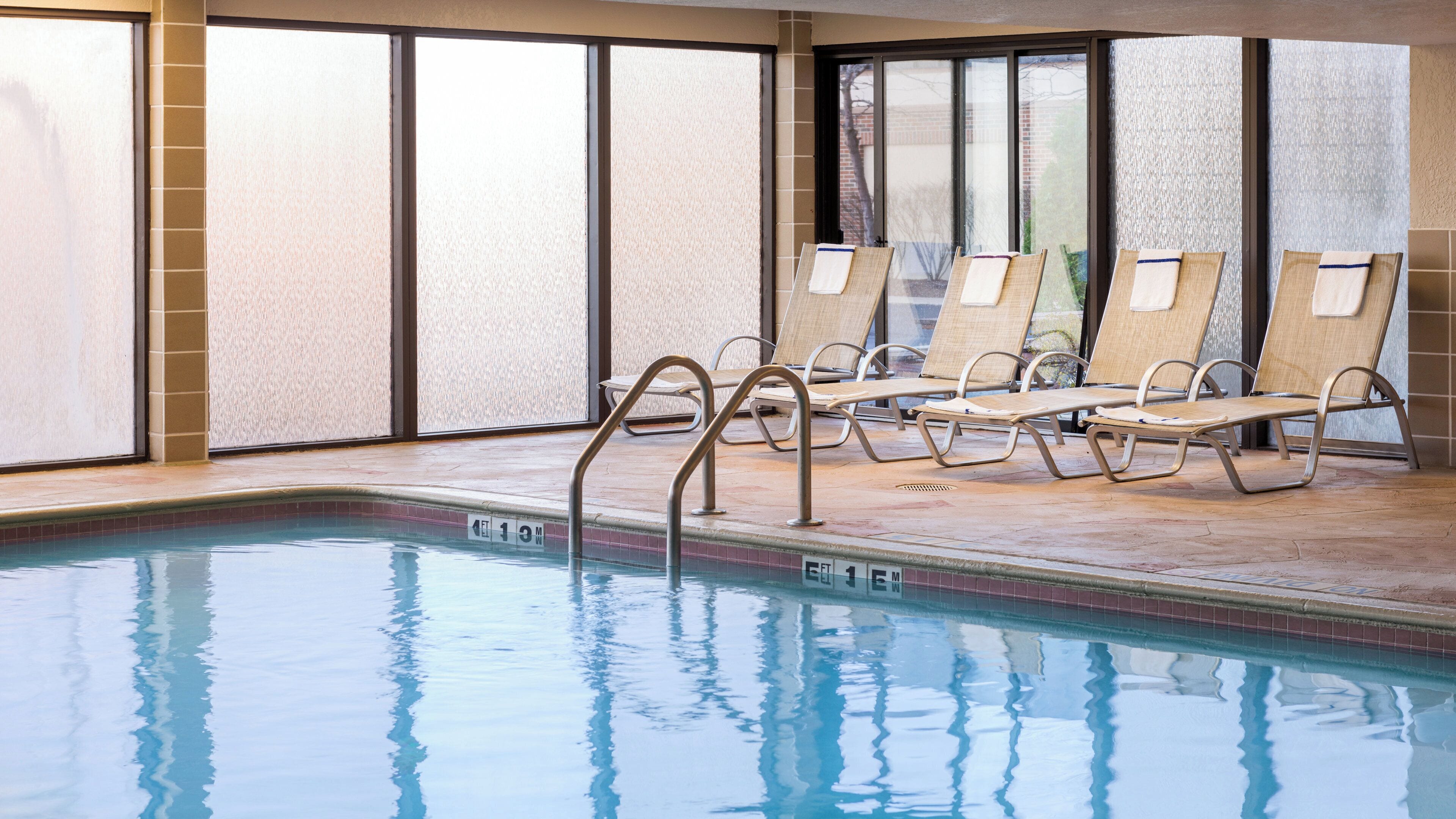 Una piscina interior con agua cristalina, una escalera de piscina y varias sillas de descanso con toallas.