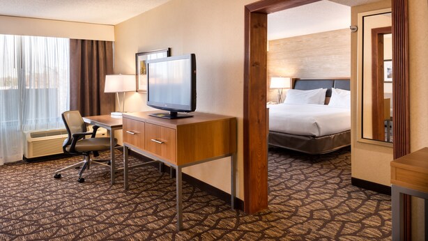 A hotel room with a desk, chair, television, bed, and a view through a door. - Holiday Inn Hotel & Suites Warren by IHG (Warren)
