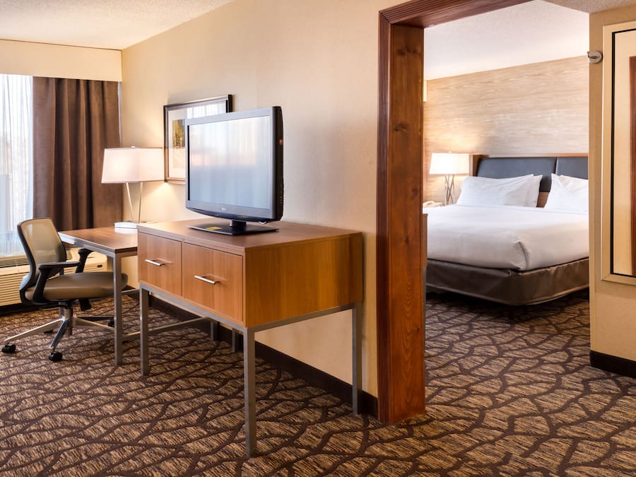 Habitación de hotel con escritorio, silla, televisor, cama y vista a través de una puerta.
