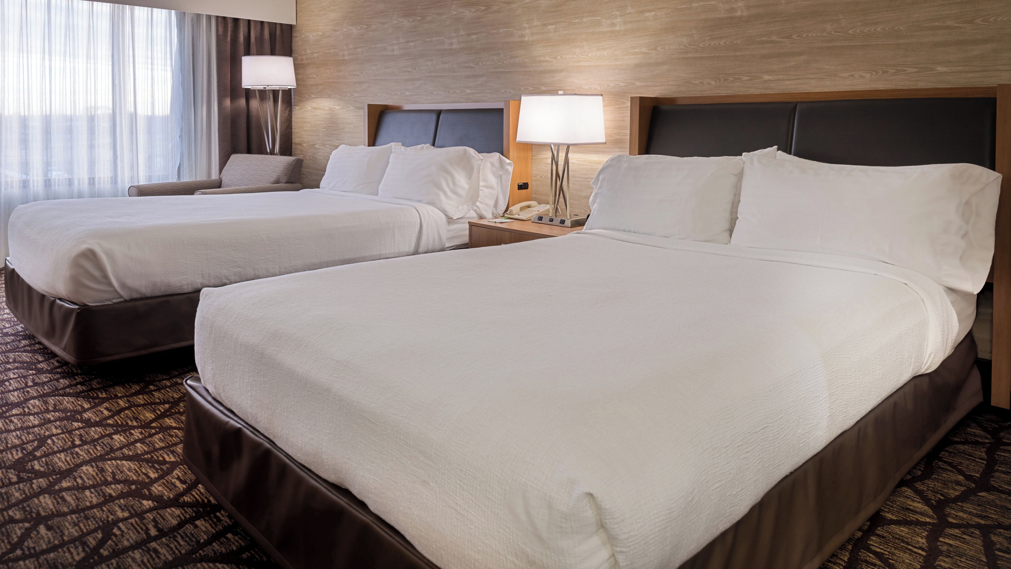 Een hotelkamer met twee bedden, een nachtkastje met een lamp en een kamerbreed tapijt met een patroon.