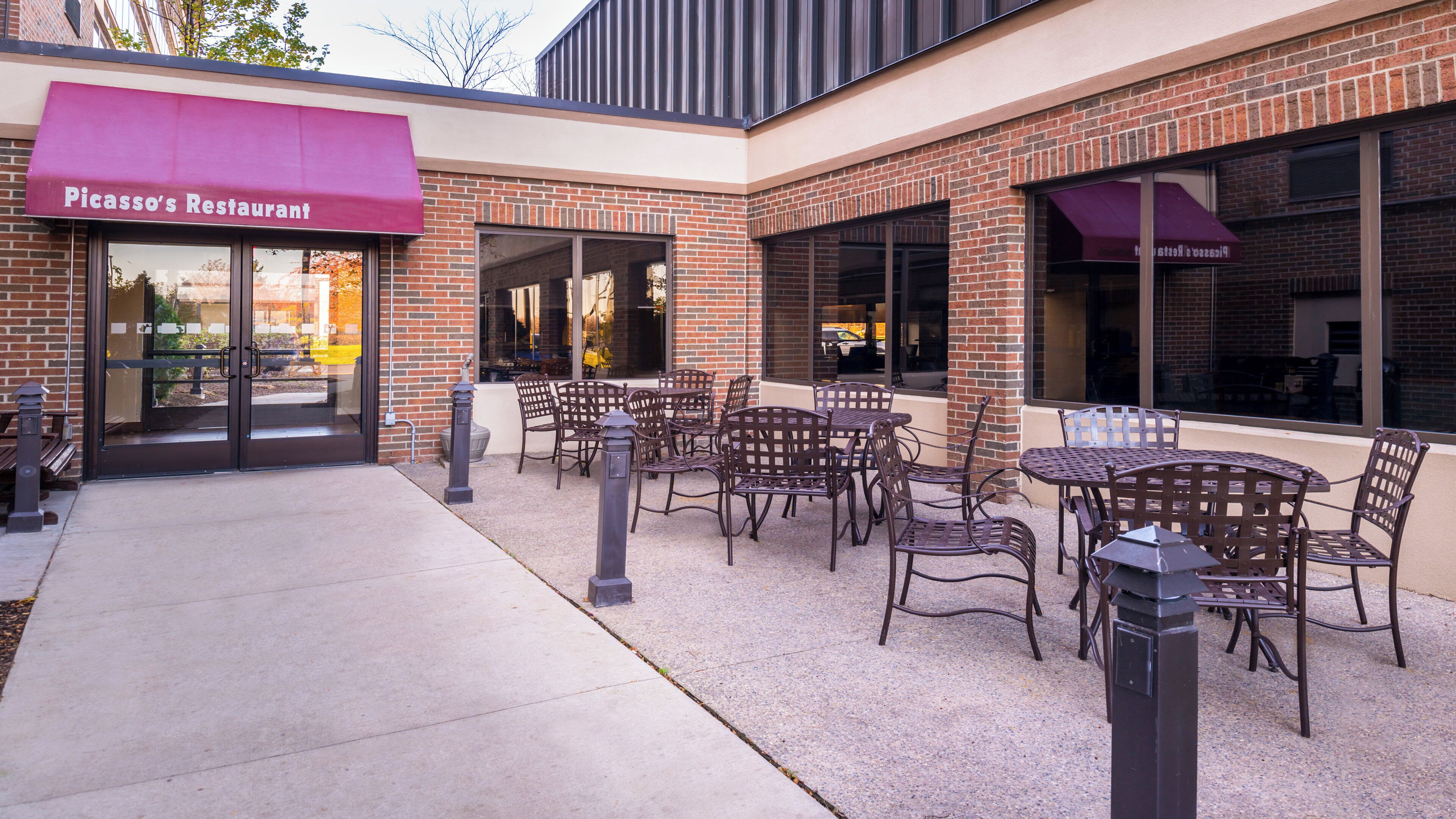 An outdoor seating area with tables and chairs, a brick building, and a storefront with a red awning.