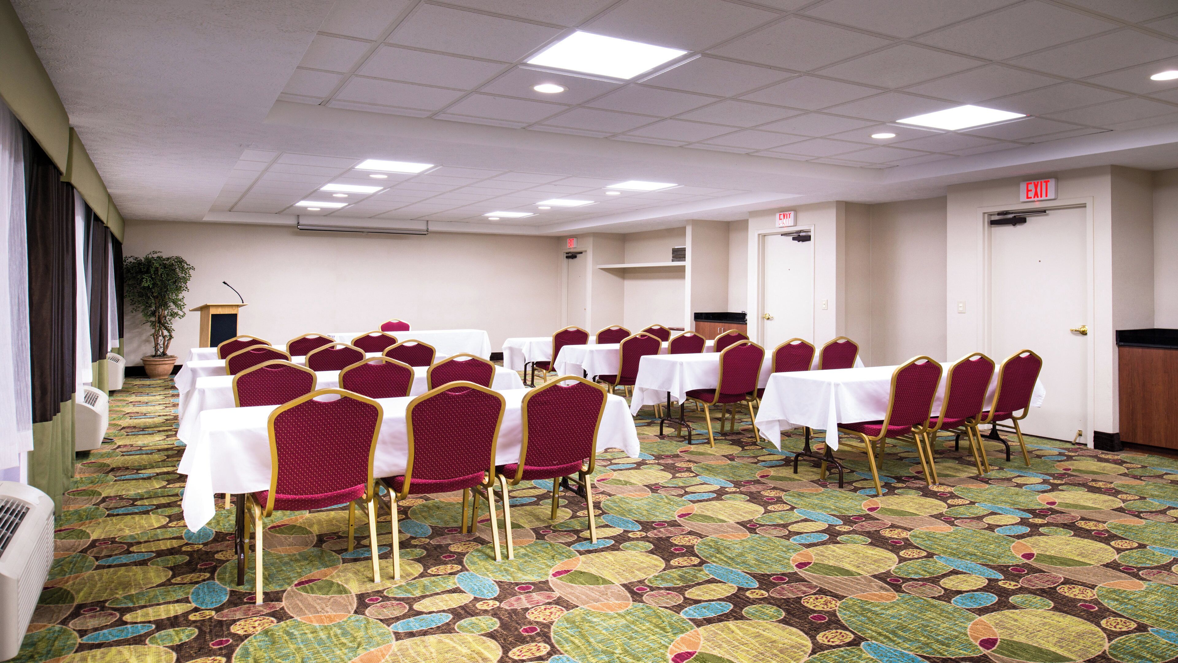 A conference room with tables and chairs, carpeted floor, and ceiling lights.