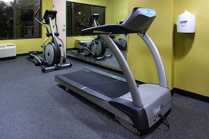 Uma academia com esteira, bicicleta ergométrica e dispensador de Purell.