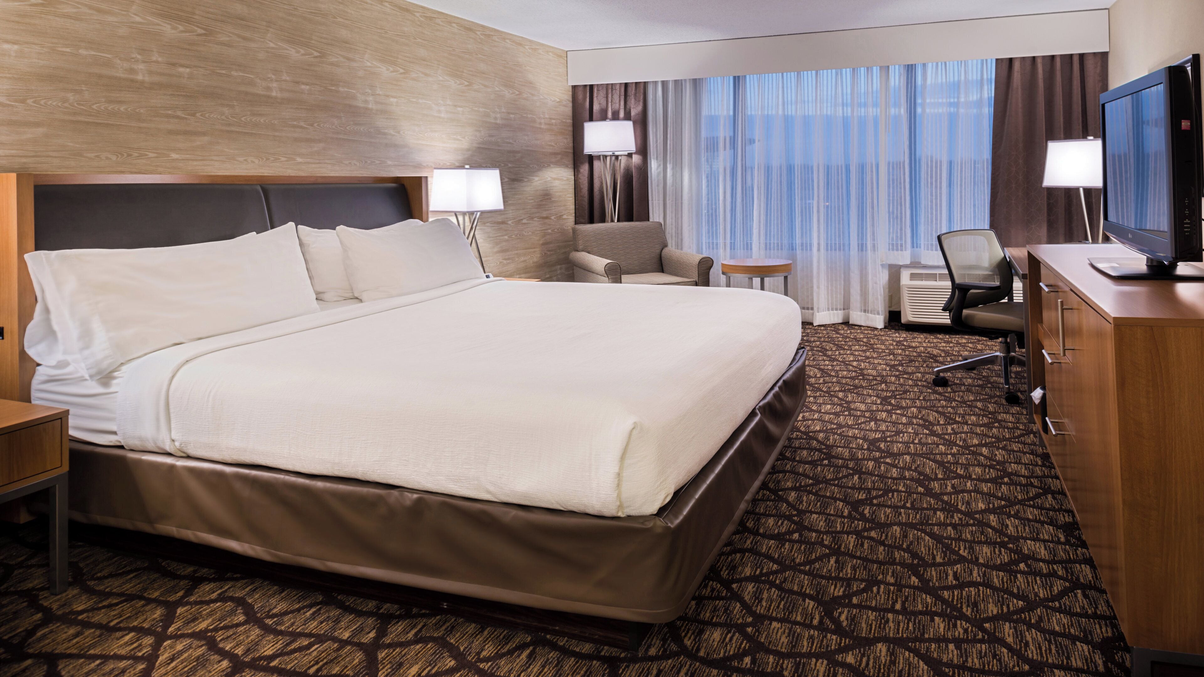 A hotel room with a large bed, a desk, a chair, and a television.