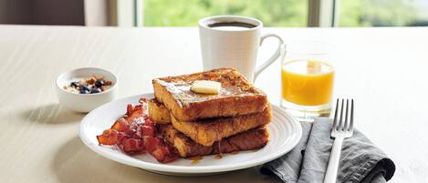 A breakfast plate with French toast, bacon, and a small bowl of blueberries.
