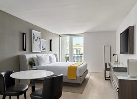 A modern hotel room with a bed, a desk, a chair, a round table, and artwork on the wall.