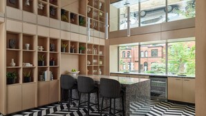A modern kitchen with a black and white patterned floor, a central island with bar stools, and a large window offering a view of a red brick building. - One Washington Circle DC, Tapestry Collection by Hilton (Washington)