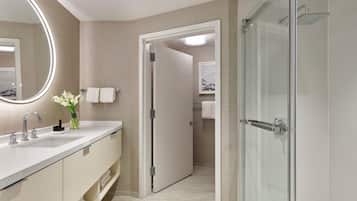 A modern bathroom with a glass shower, a vanity with a mirror, and a door leading to another room.