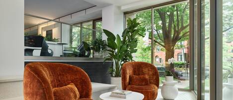 A modern living room with two large velvet armchairs, a white coffee table, and a large window with a view of trees and buildings.