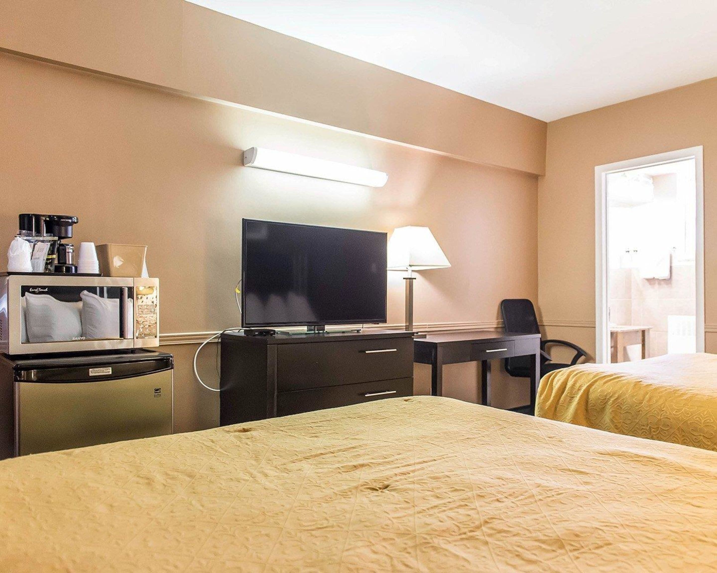 A hotel room with a bed, a desk with a computer, a television, and a minibar.