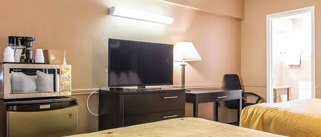 A hotel room with a bed, a desk with a computer, a television, and a minibar.