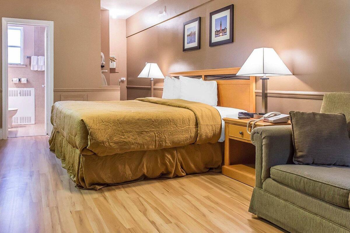 Een hotelkamer met een bed, nachtkastje, lamp en een groene fauteuil.