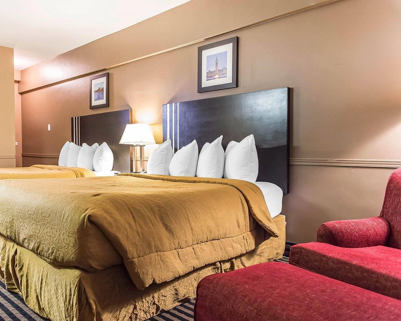 Una habitación de hotel con una cama grande, un escritorio, una silla y dos cuadros en la pared.