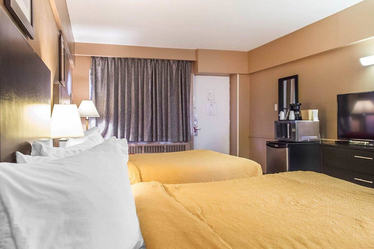 Een hotelkamer met twee bedden, een televisie, een bureau met koffiezetapparaat, en een raam met gordijnen.