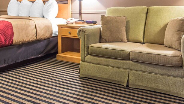 Une chambre d’hôtel avec un lit, un canapé vert, une table de chevet avec une lampe et un tableau encadré au mur.