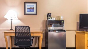 Une chambre d’hôtel compacte comprenant un bureau, un fauteuil de bureau, un réfrigérateur avec un micro-ondes et une télévision.