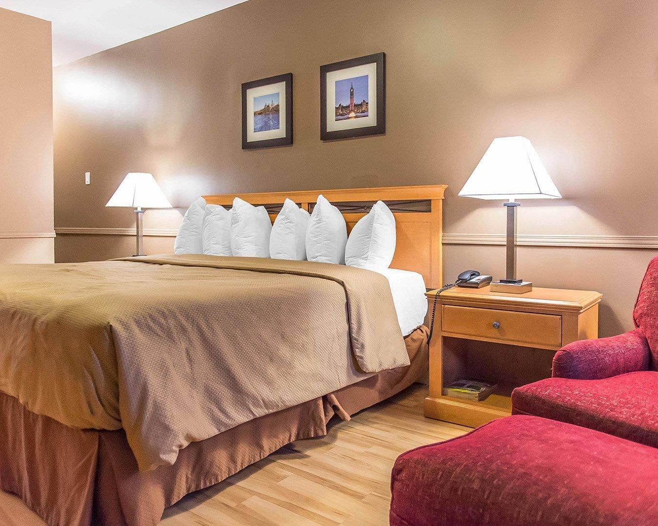 A hotel room with a bed, two bedside lamps, a nightstand, a chair, and two framed pictures on the wall.