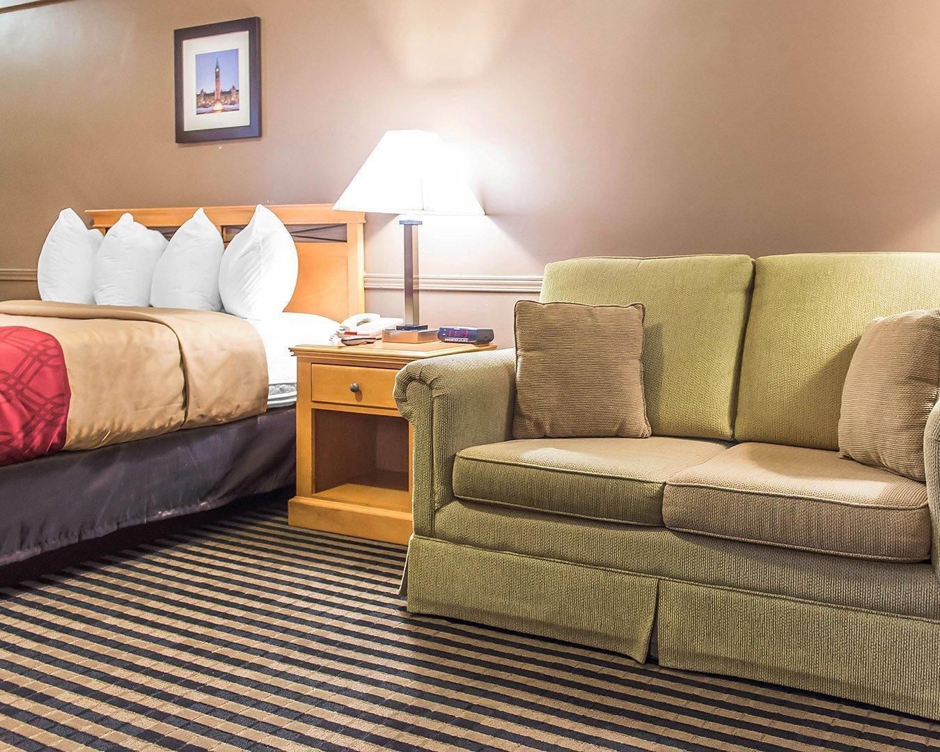Una habitación de hotel con una cama, un sofá verde, una mesita de noche con una lámpara y un cuadro en la pared.