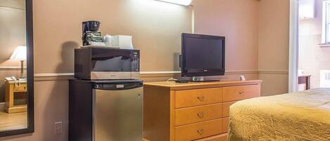 A hotel room with a bed, a desk with a microwave, a refrigerator, a television, and a dresser.