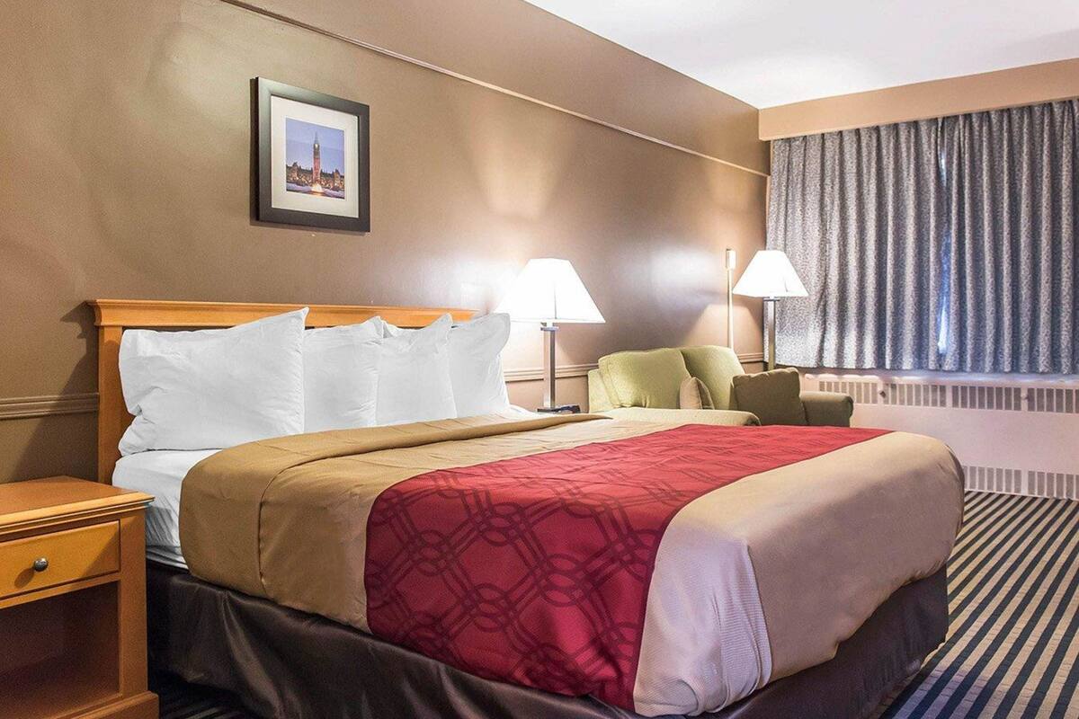 Een hotelkamer met een bed, nachtkastjes, lampen, een raam met gordijnen en een ingelijst beeld aan de muur.