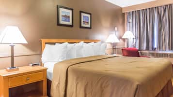Una habitación de hotel con una cama, dos lámparas de noche, una mesita de noche, una silla roja y dos cuadros en la pared.