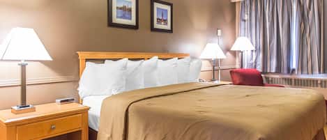 Una habitación de hotel con una cama, dos lámparas de noche, una mesita de noche, una silla roja y dos cuadros en la pared.