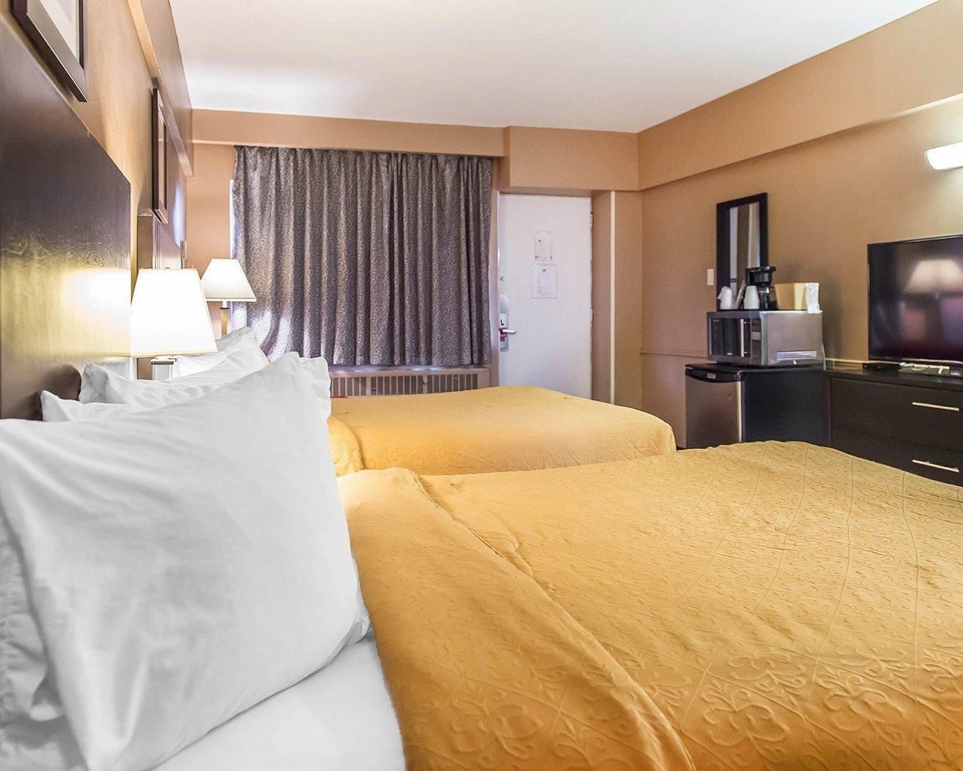 A hotel room with two beds, a television, a coffee machine, and a desk.