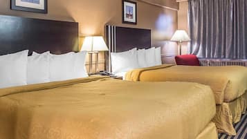 Quarto de hotel com duas camas, uma cadeira vermelha, mesa de cabeceira com abajur e quadros nas paredes.
