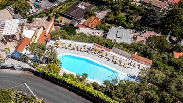 Una vista aerea di una zona residenziale con una piscina circondata da poltroncine e ombrelloni.
