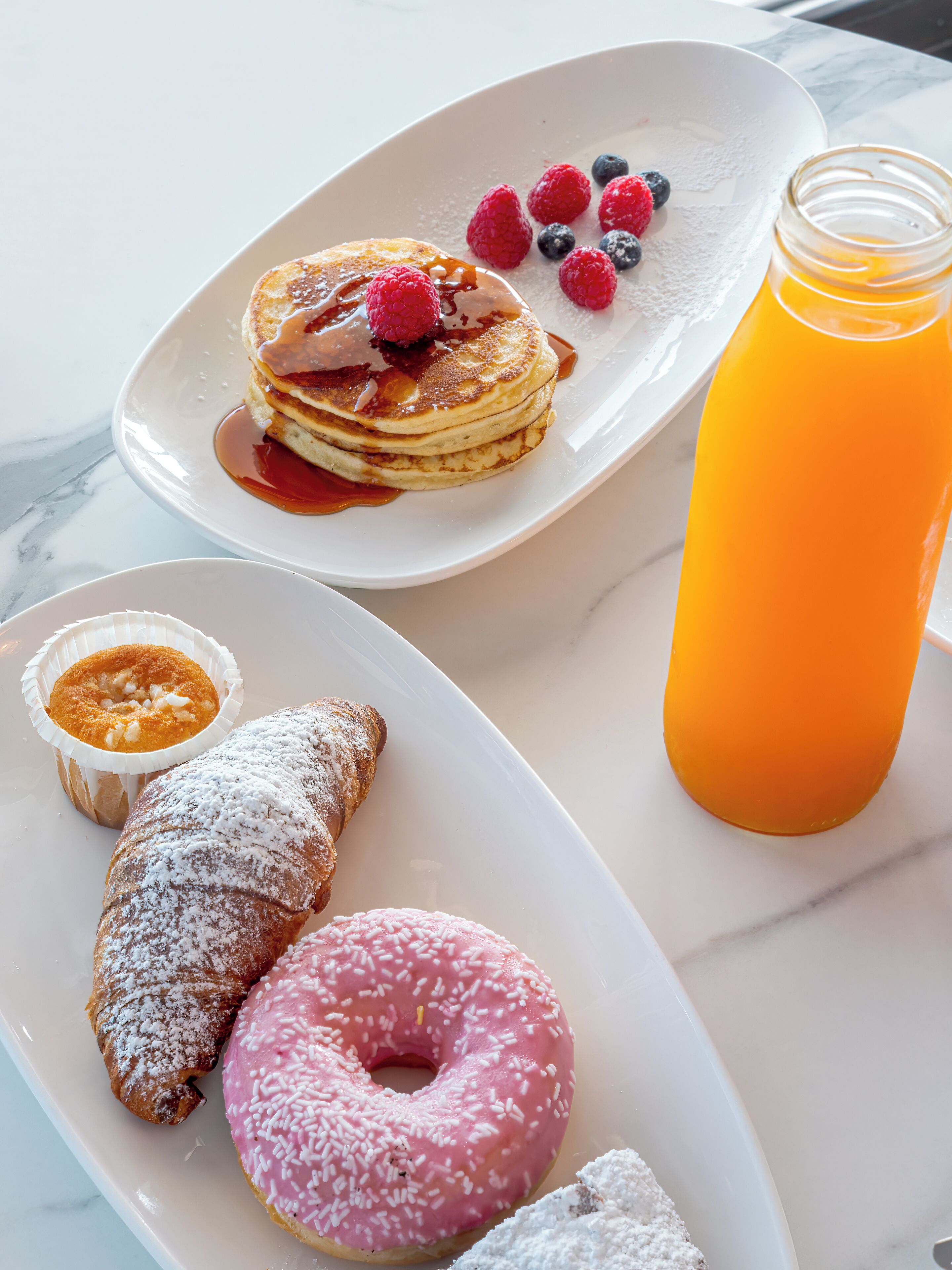 Une assiette de petit-déjeuner avec des crêpes, des fruits rouges, un beignet et un verre de jus d’orange.