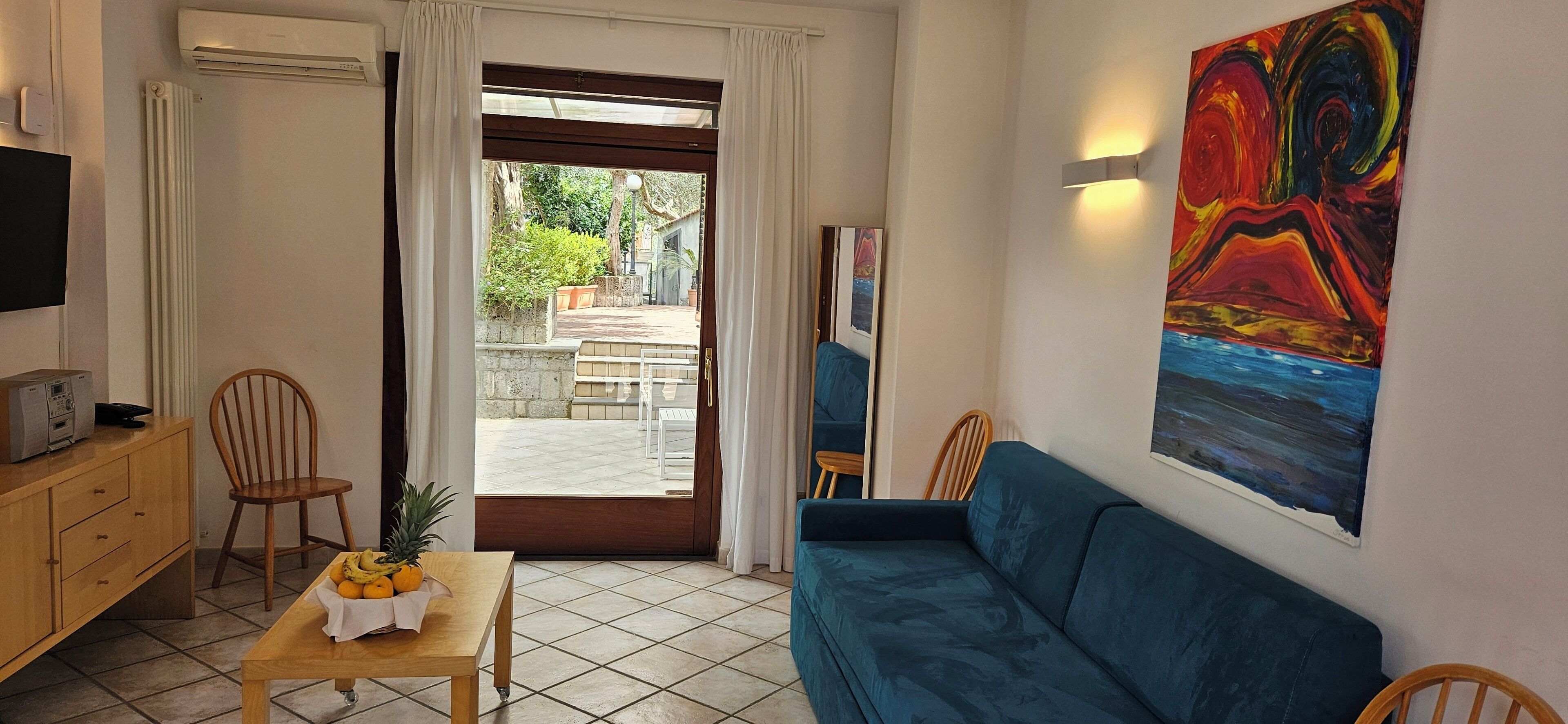 A living room with a blue sofa, a wooden table with fruit, a TV, and a painting on the wall.