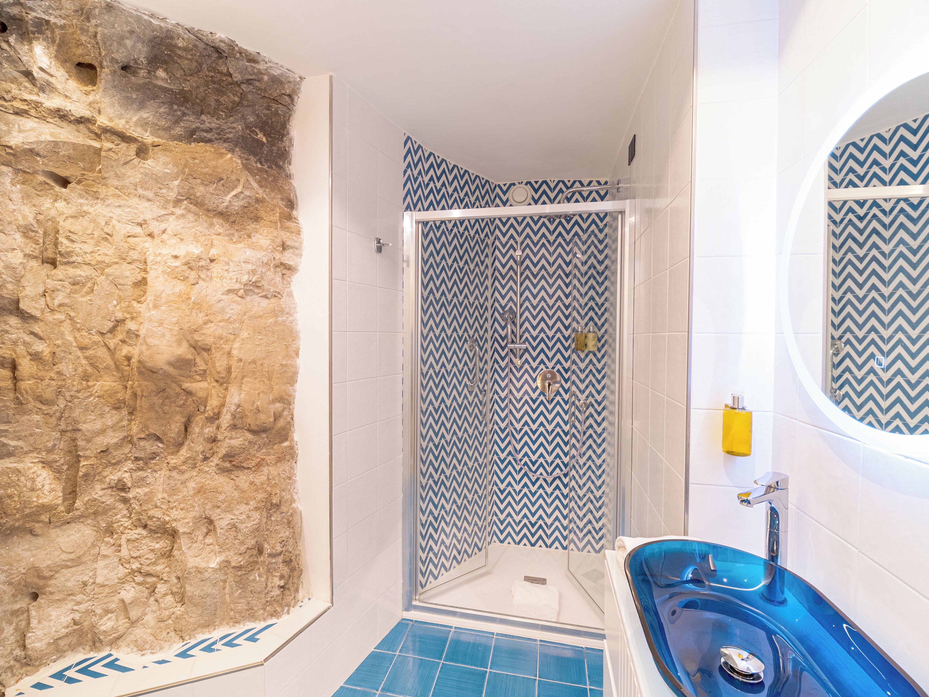 A bathroom with a stone wall, a shower with blue and white chevron-patterned tiles, and a blue-tub sink.