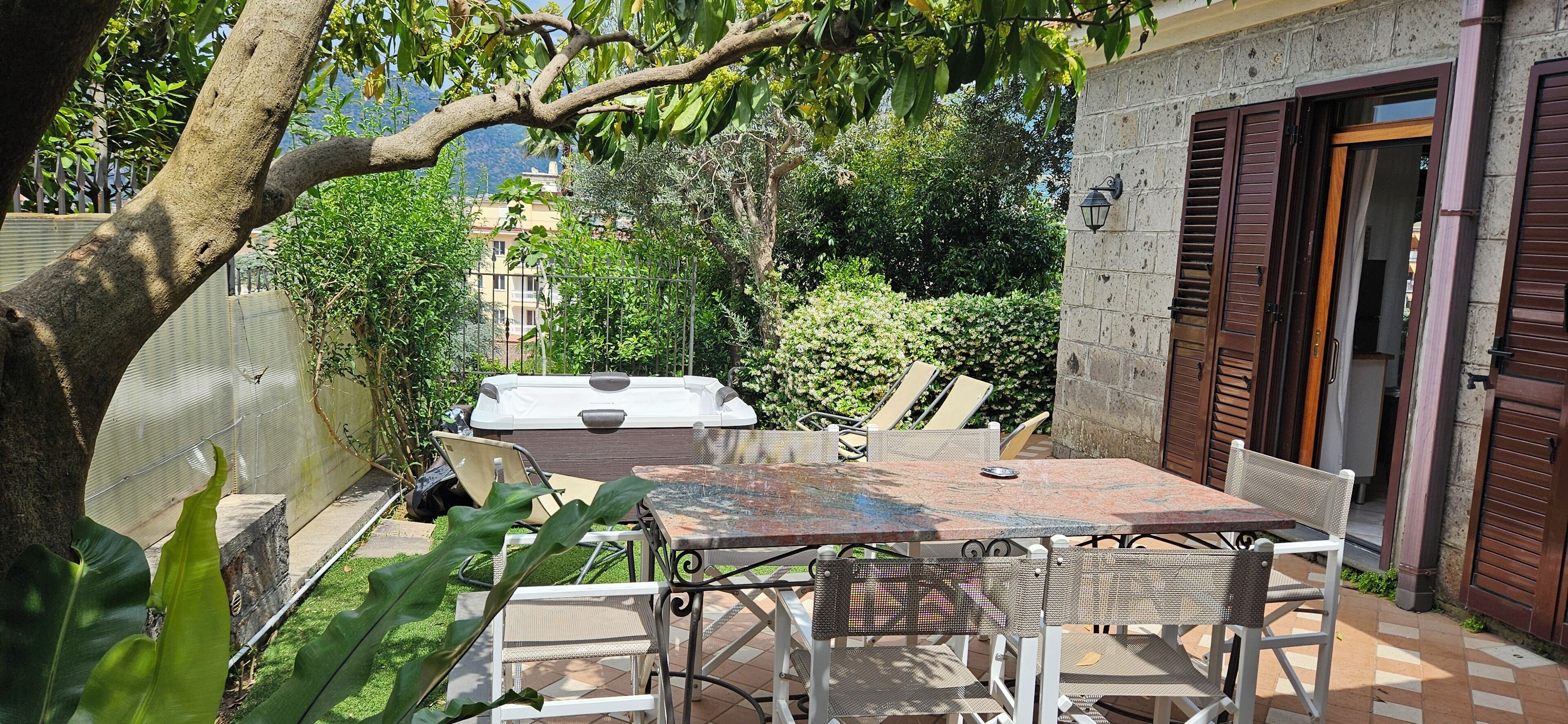 Une terrasse extérieure avec une table et des chaises, entourée de verdure et offrant une vue sur les bâtiments en arrière-plan.
