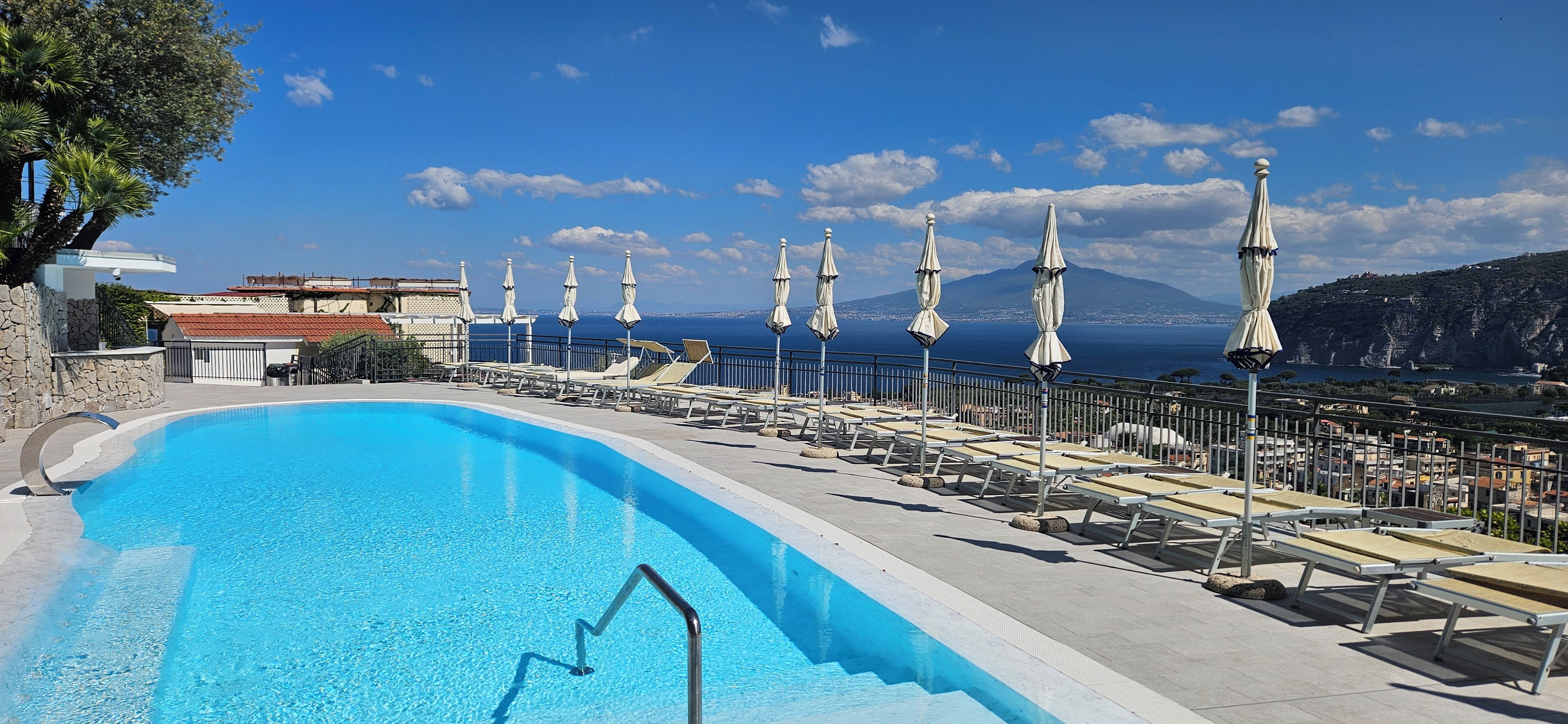 Una piscina con lettini e ombrelloni, con vista su una località costiera e montagne.