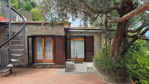 Un edificio de piedra con puerta de madera y ventanas con contraventanas, una escalera metálica y un banco.