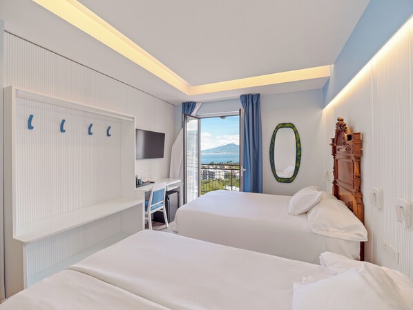 Habitación de hotel con dos camas, un escritorio, un televisor y vistas a la ciudad y montañas.