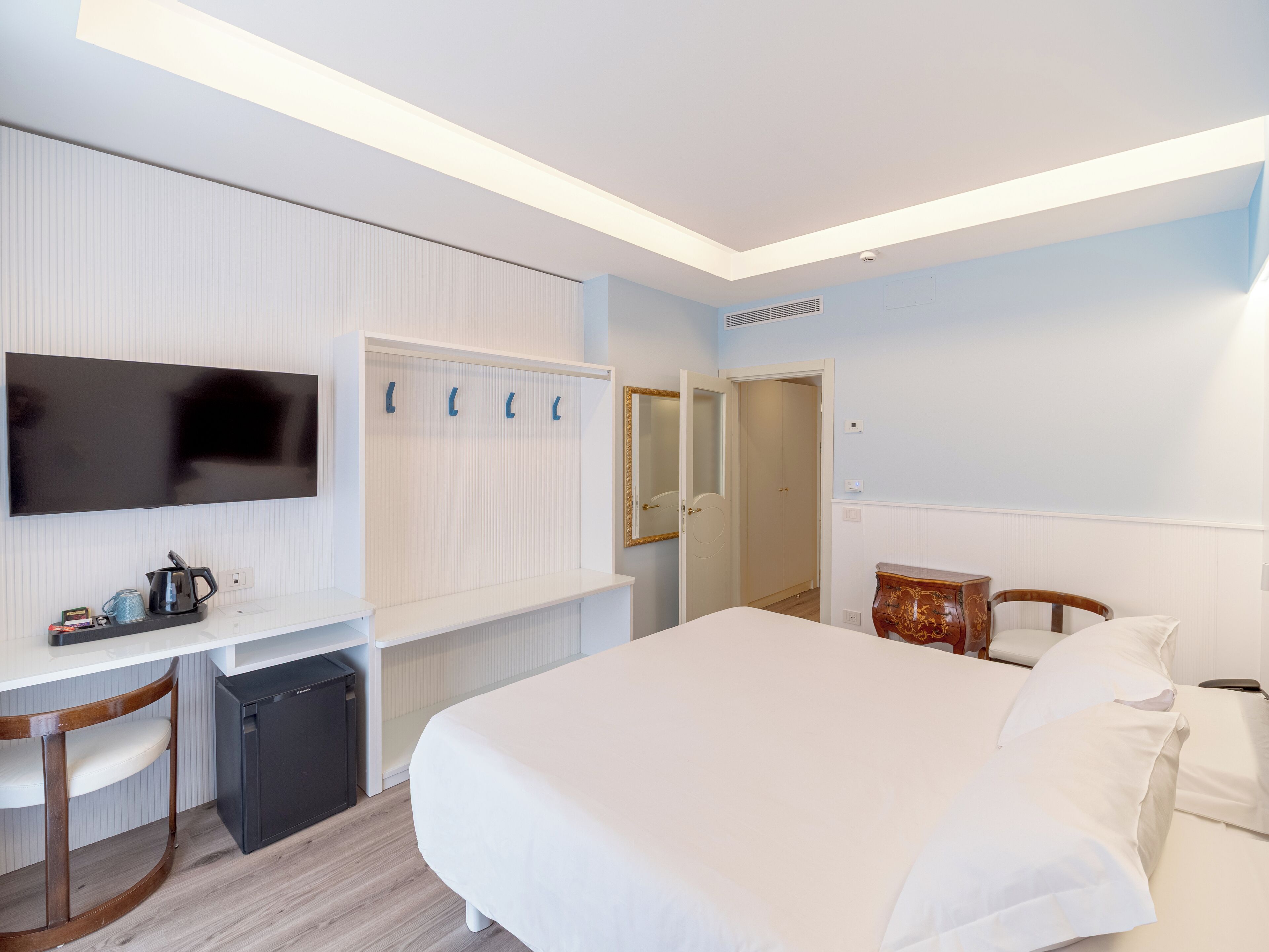 A hotel room with a bed, a desk, a television, a wardrobe, and a mirror.