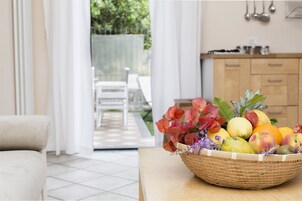 A wicker basket filled with fruits and flowers on a table in a well-lit room with a view of a patio area.