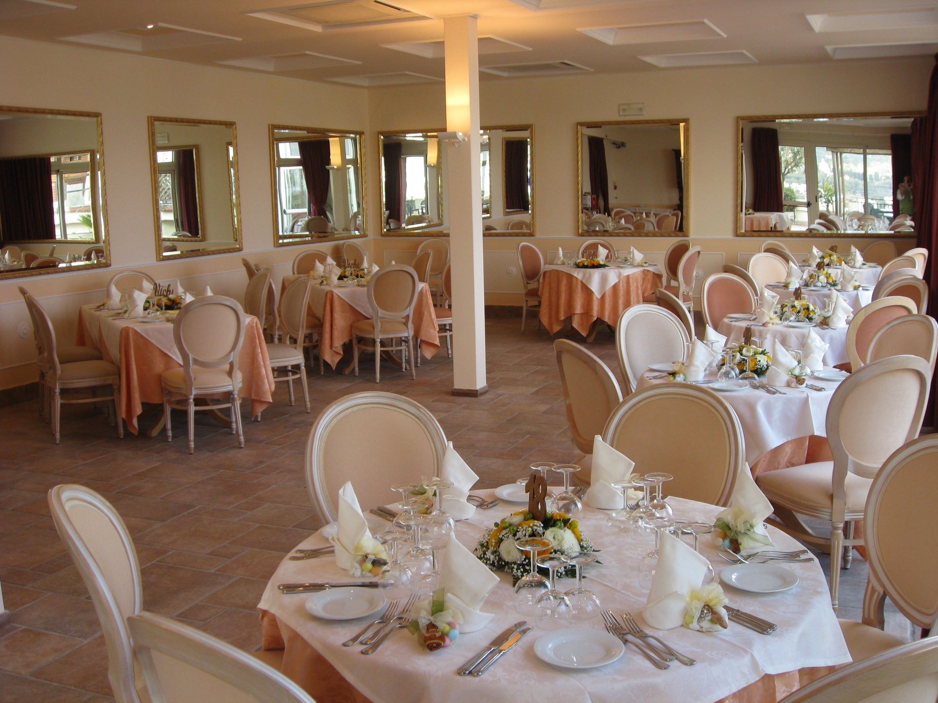 A banquet hall with multiple round tables set for dining, each with white tablecloths and floral centerpieces.